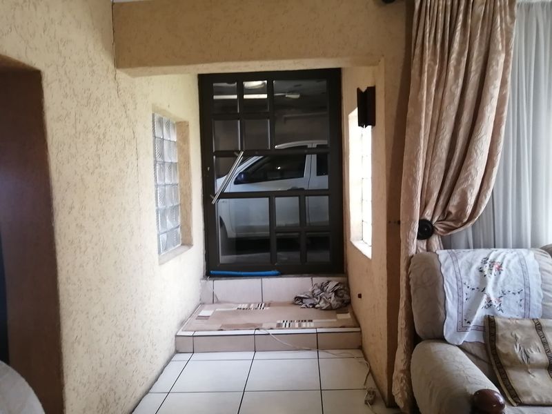An entrance area featuring tiled flooring, glass block windows, and a security door, showing signs of wear on the textured wall finish.