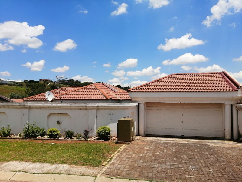 Front exterior view of the property featuring a tiled roof, a single garage door, and a paved driveway with a boundary wall.