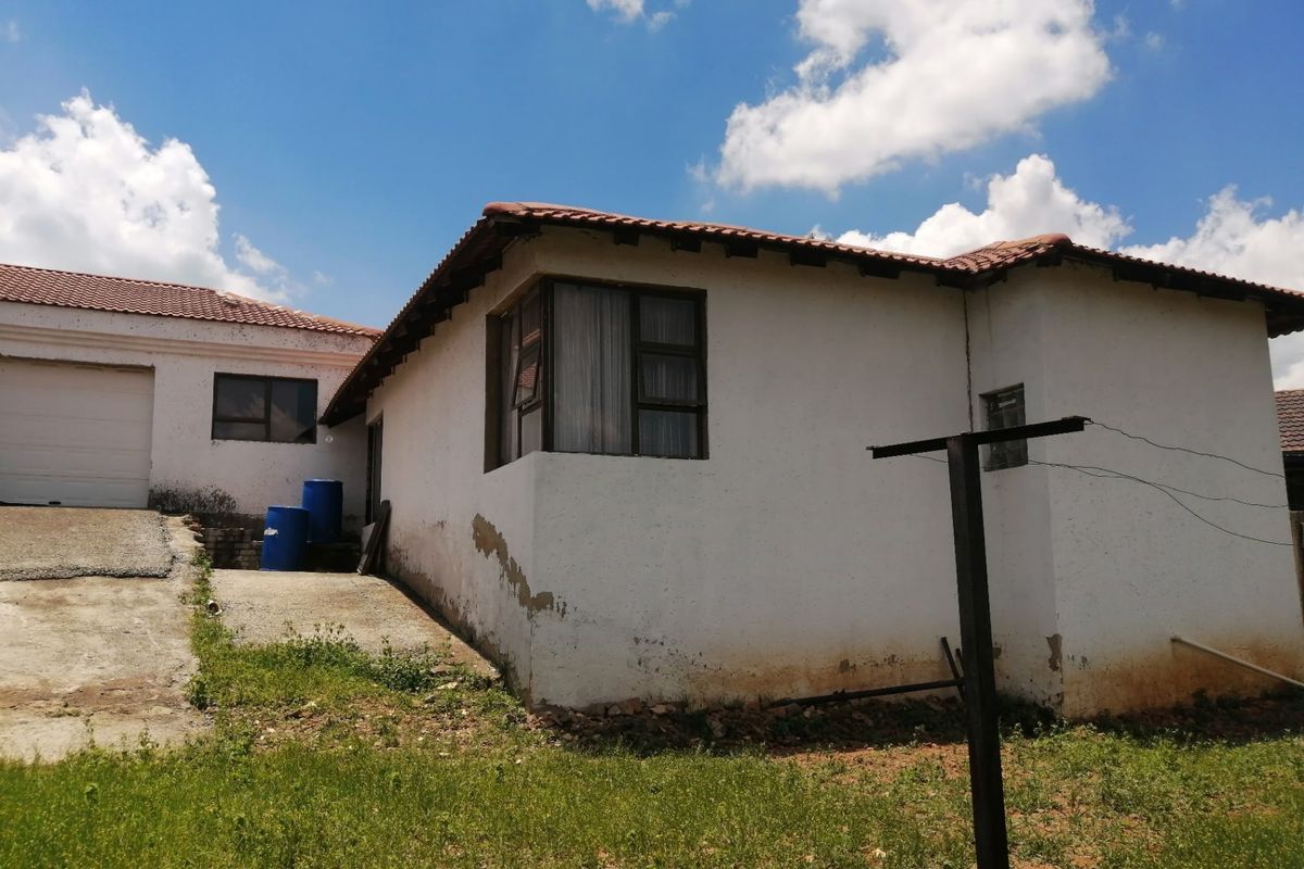 Rear view of the property showing the exterior facade, garage access, and surrounding yard area with visible signs of wear and maintenance requirements.
