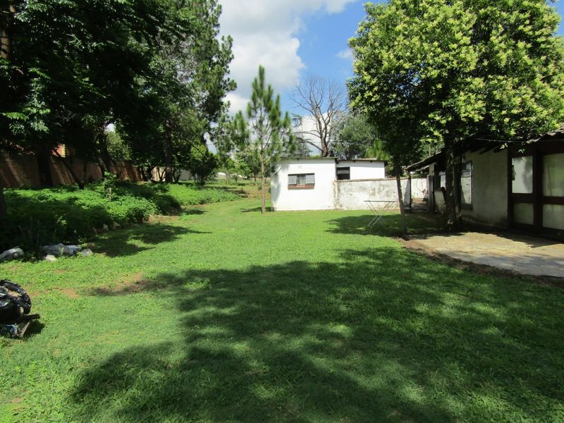 A spacious rear garden featuring a large lawn, mature trees, a paved patio area, and a detached outbuilding structure.