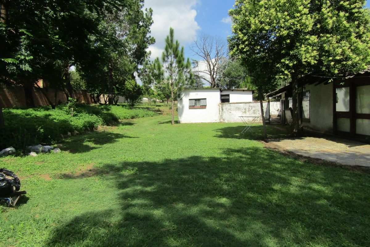 A spacious rear garden featuring a large lawn, mature trees, a paved patio area, and a detached outbuilding structure.