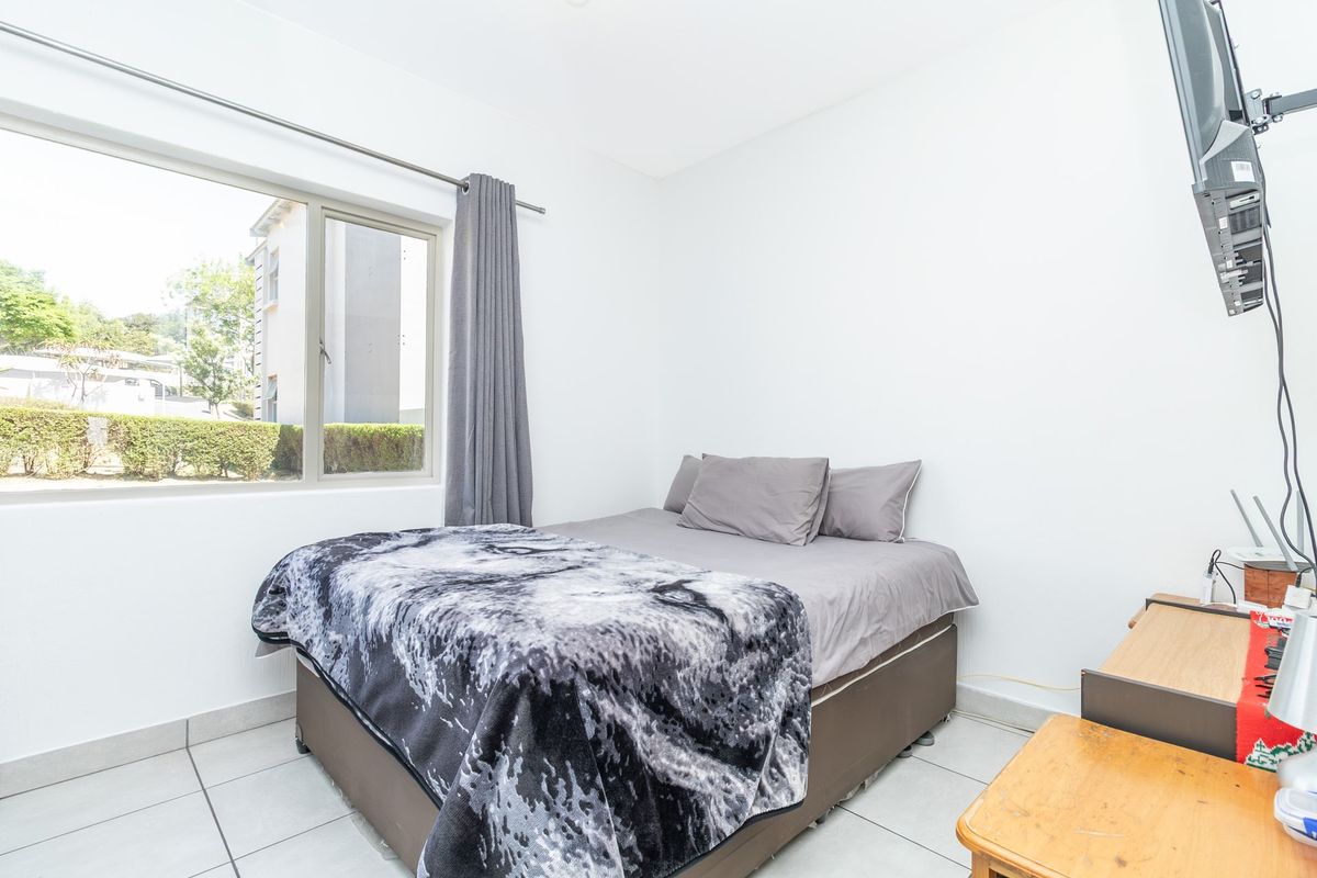 A functional bedroom featuring tiled flooring, a large window with curtain rail, and a wall-mounted television bracket.