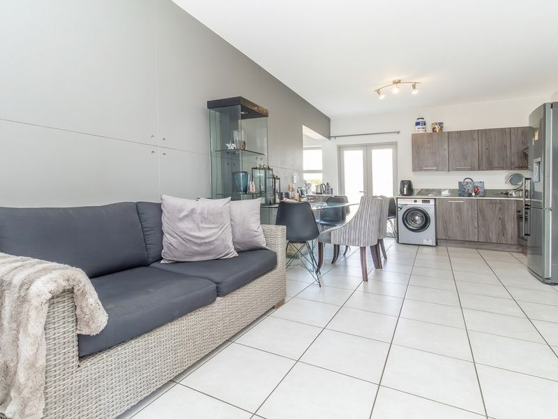 Open-plan living and kitchen area featuring tiled flooring, modern wood-finish cabinetry, and direct access to an outdoor space through glass doors.