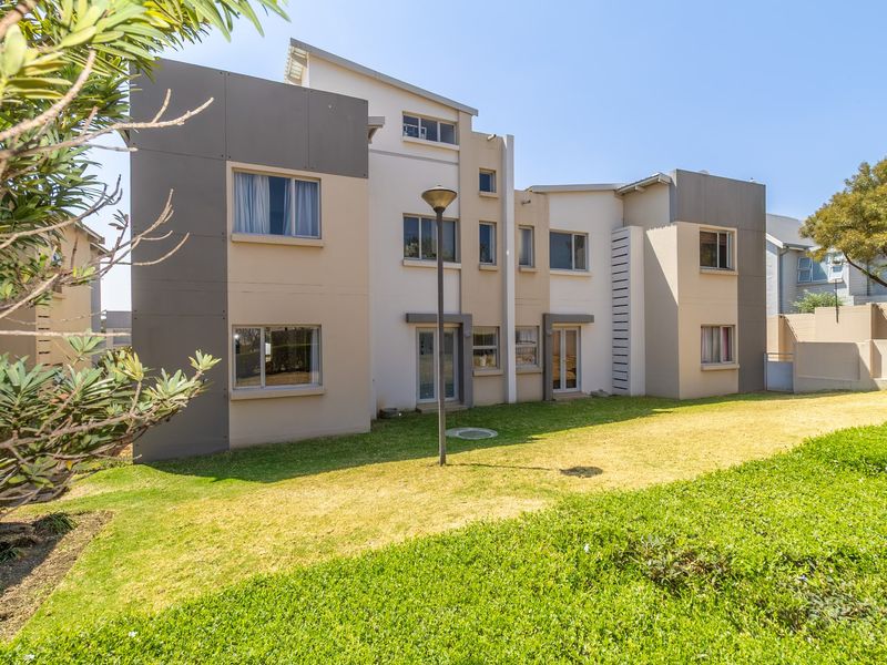 Rear view of a modern multi-story apartment building featuring a well-maintained lawn and contemporary architectural facade.