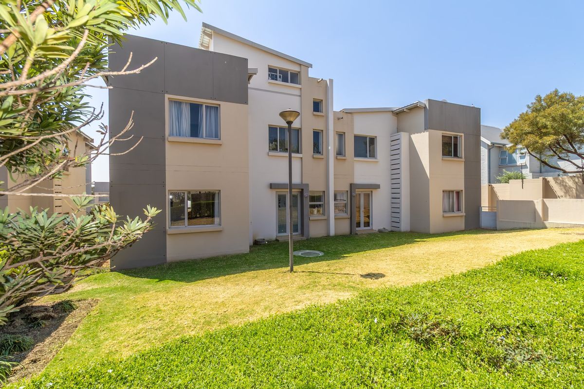 Rear view of a modern multi-story apartment building featuring a well-maintained lawn and contemporary architectural facade.