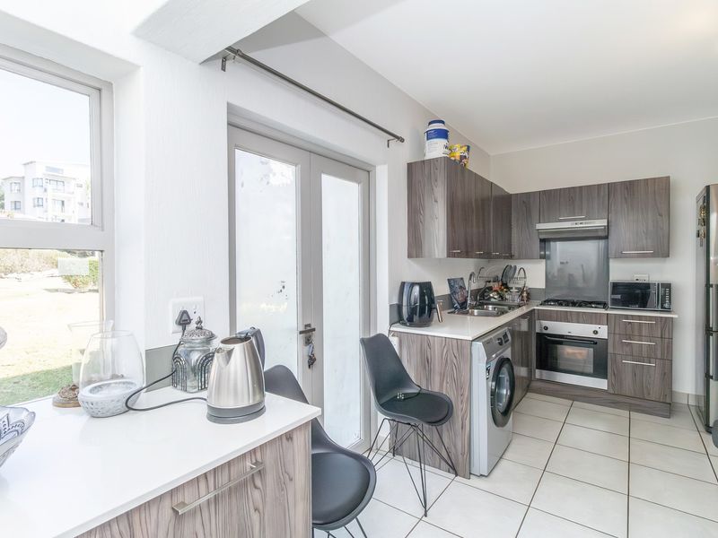 Modern kitchen featuring wood-grain cabinetry, integrated oven and hob, tiled flooring, and direct access to the exterior through a double glass door.