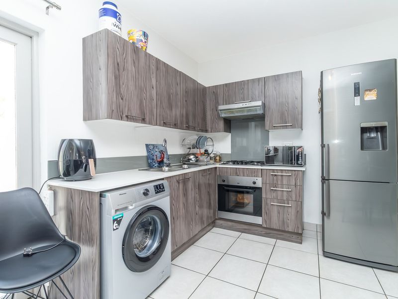 Modern kitchen featuring wood-grain laminate cabinetry, stainless steel appliances, built-in oven, gas hob, and tiled flooring with direct access to an outdoor area.