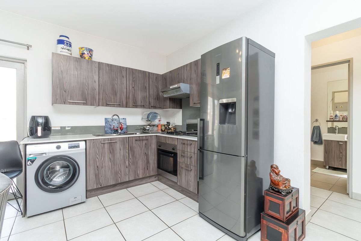 Modern kitchen featuring dark wood-grain cabinetry, integrated oven, extractor fan, and tiled flooring, with an adjacent view into the bathroom area.