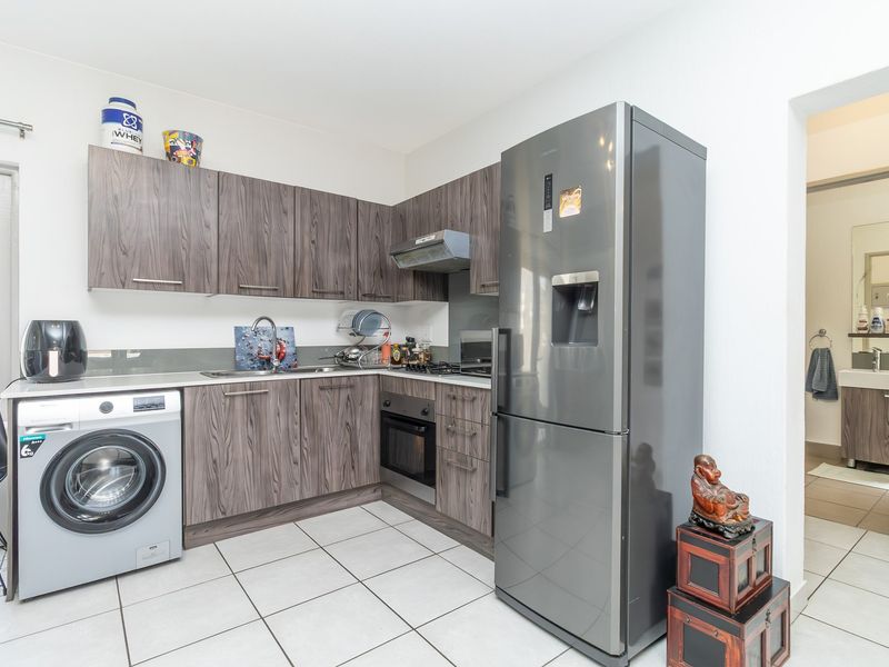 Modern kitchen featuring dark wood-grain cabinetry, integrated oven, extractor fan, and tiled flooring, with an adjacent view into the bathroom area.