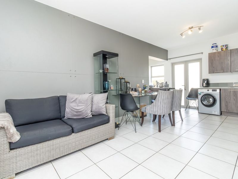 Open-plan living and kitchen area featuring tiled flooring, modern cabinetry, integrated laundry appliance, and a distinctive panelled feature wall.