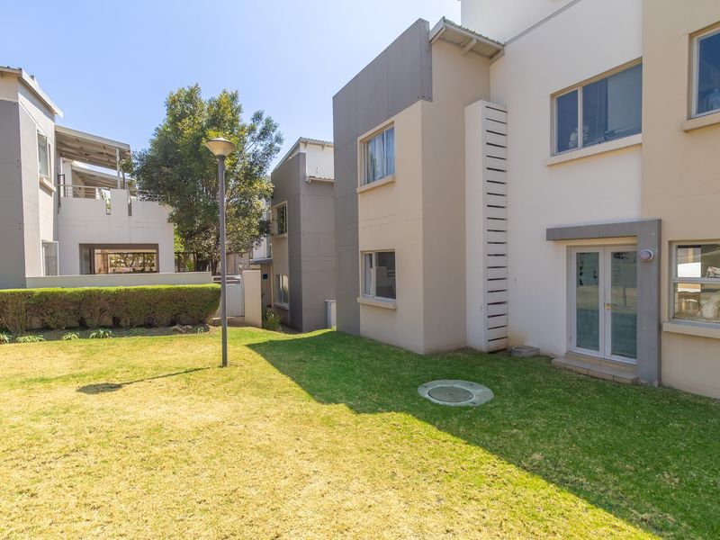 A view of the rear exterior of the apartment complex, featuring a well-maintained lawn, modern building facade, and paved access points.
