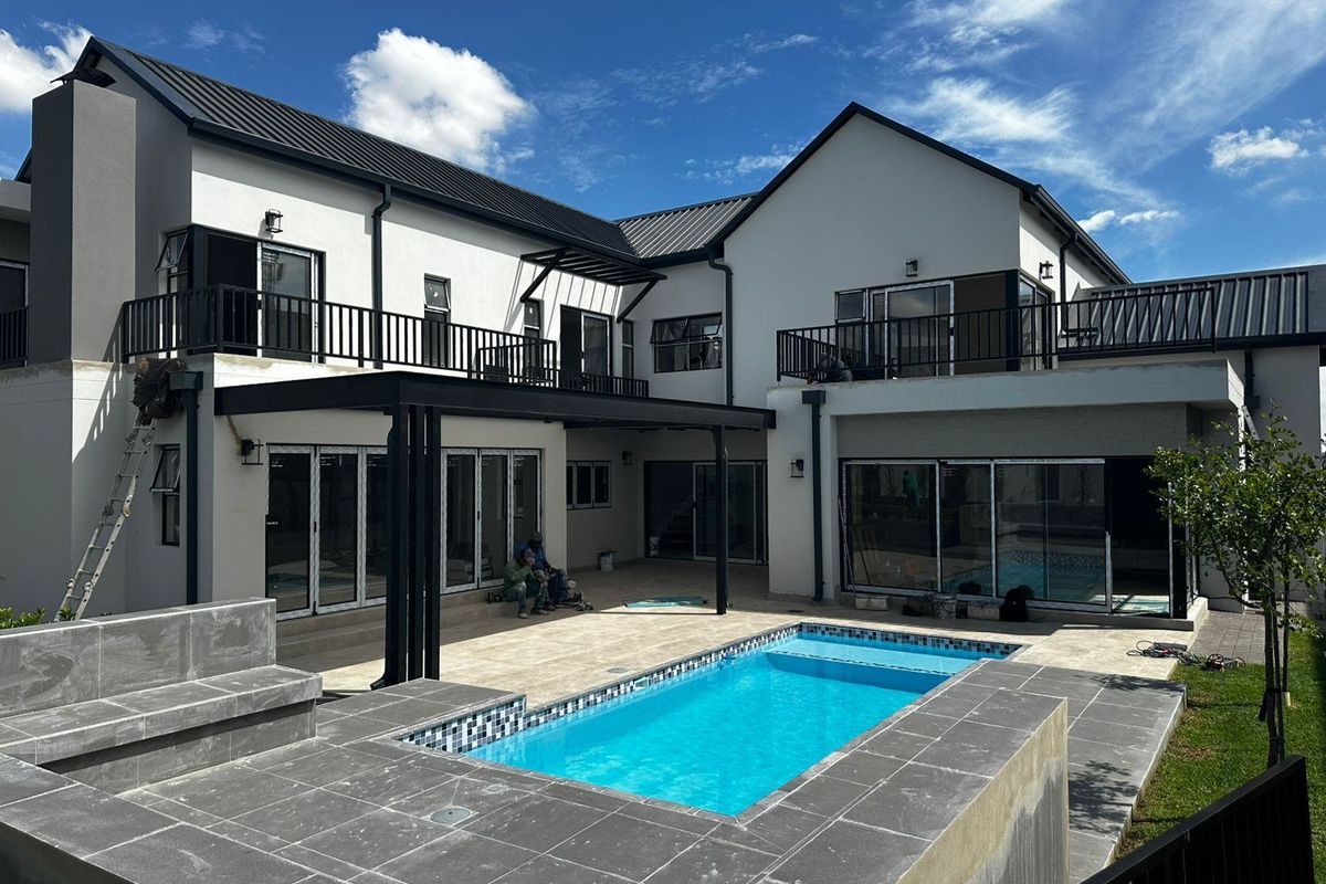 Rear exterior view of a modern two-story house featuring a swimming pool, tiled patio area, and upper-level balconies with black metal railings.