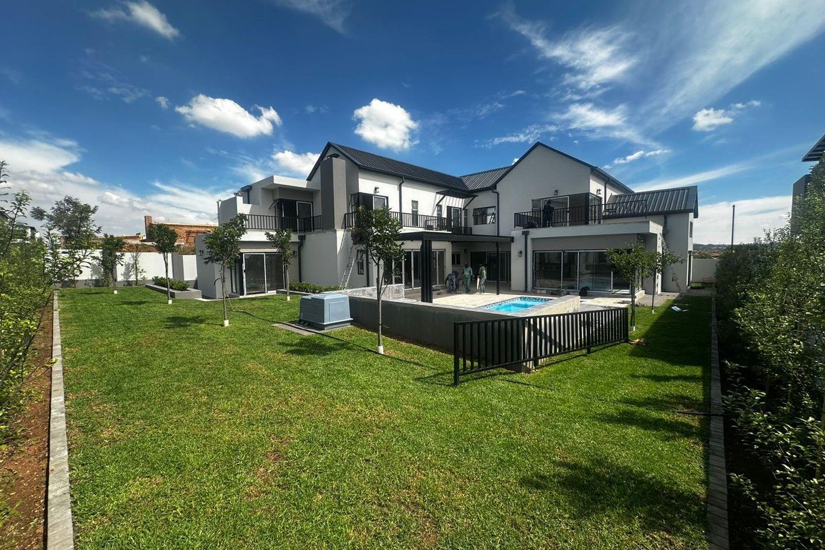 Rear view of a modern two-story house featuring a landscaped garden, swimming pool, covered patio, and upper-level balconies with sliding glass doors.