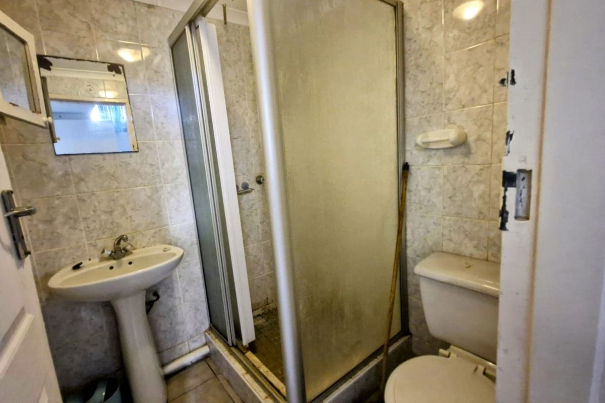 A compact bathroom featuring a pedestal basin, toilet, and shower enclosure with tiled finishes, currently requiring renovation and cosmetic updates.