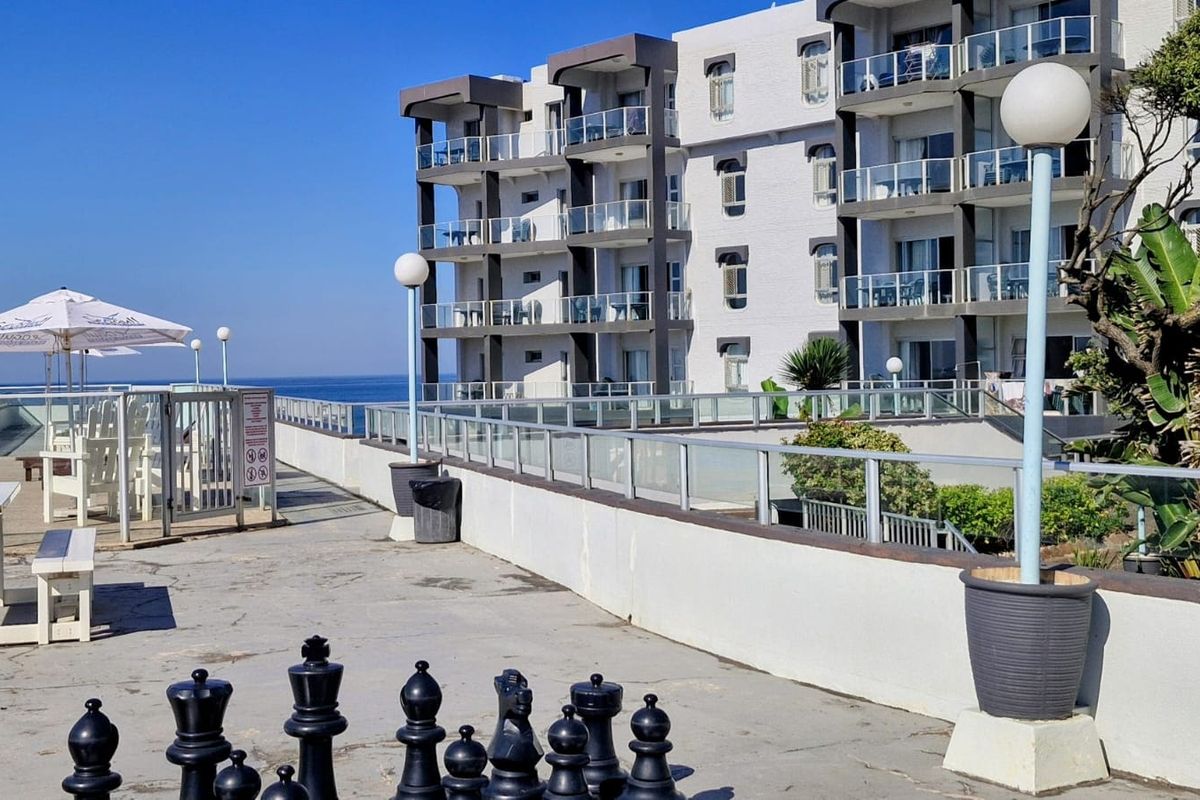 Exterior view of an apartment complex featuring a paved terrace area with glass balustrades, overlooking the ocean.