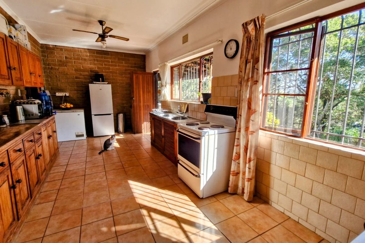 A spacious kitchen featuring wooden cabinetry, tiled flooring, exposed brick walls, and large windows with security bars, offering a functional layout with ample natural light.