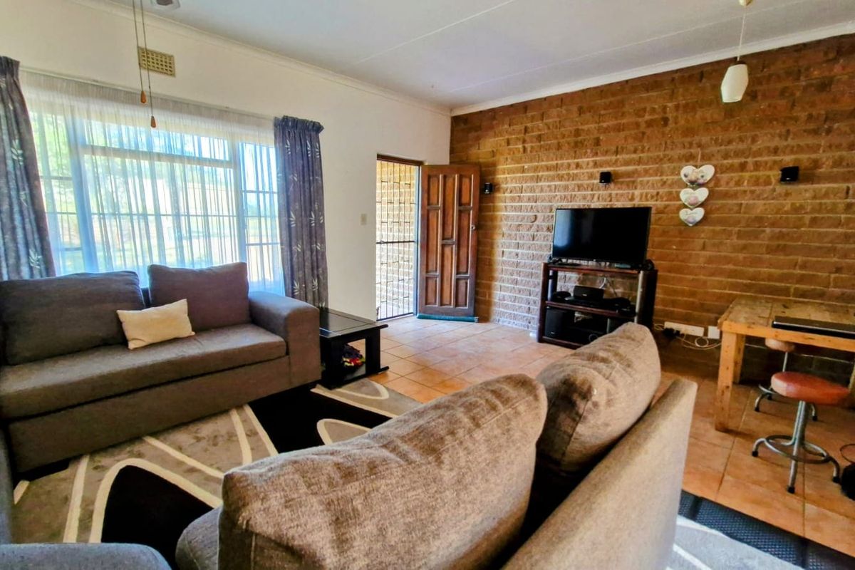 A living room featuring an exposed brick feature wall, tiled flooring, and direct access to the exterior via a timber door with security gate.