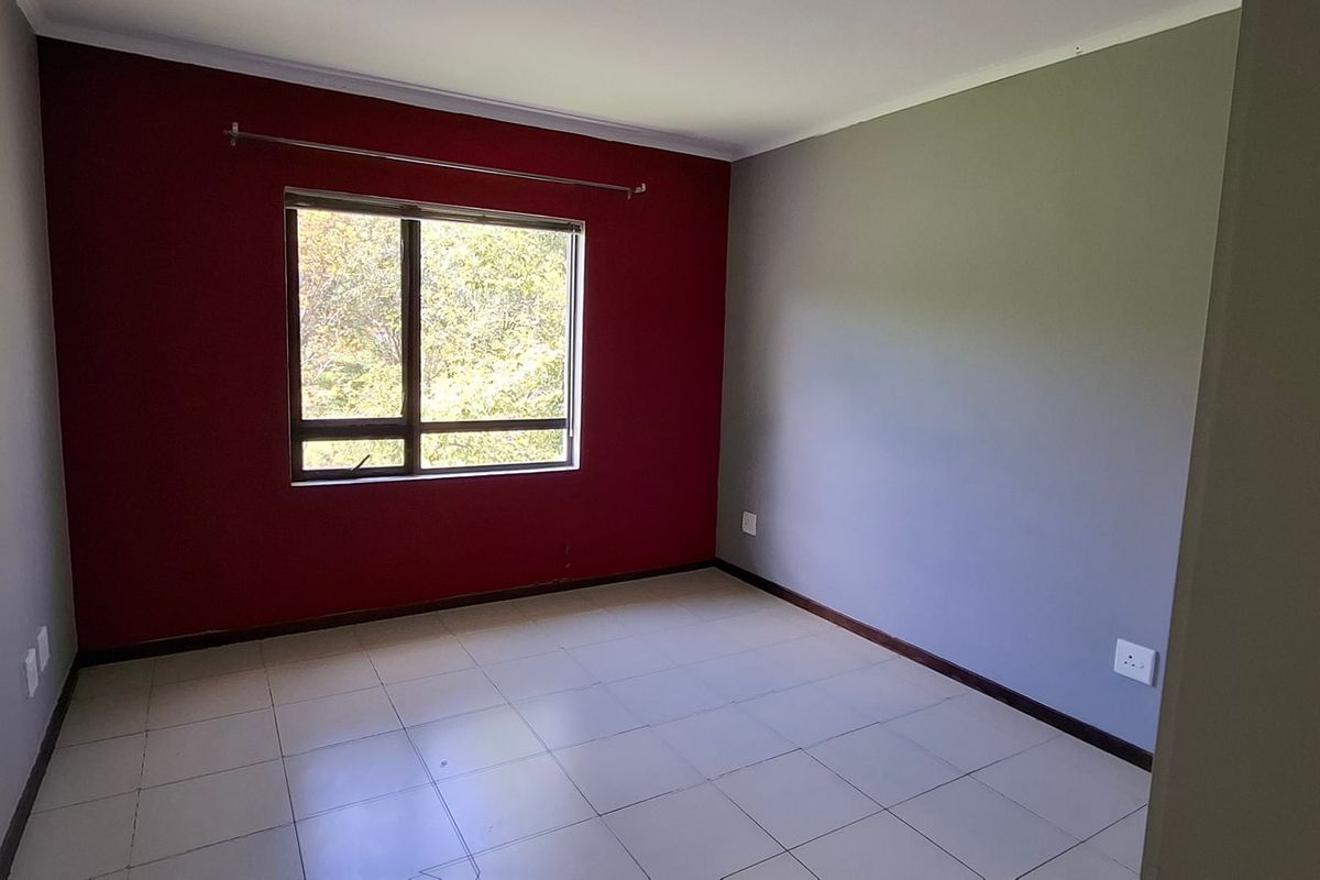 A vacant bedroom featuring tiled flooring, a large aluminium window, and a bold red accent wall.