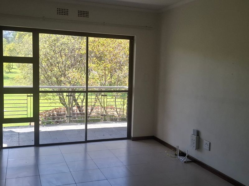 An empty living room featuring tiled flooring and a large sliding glass door providing access to a balcony with garden views.