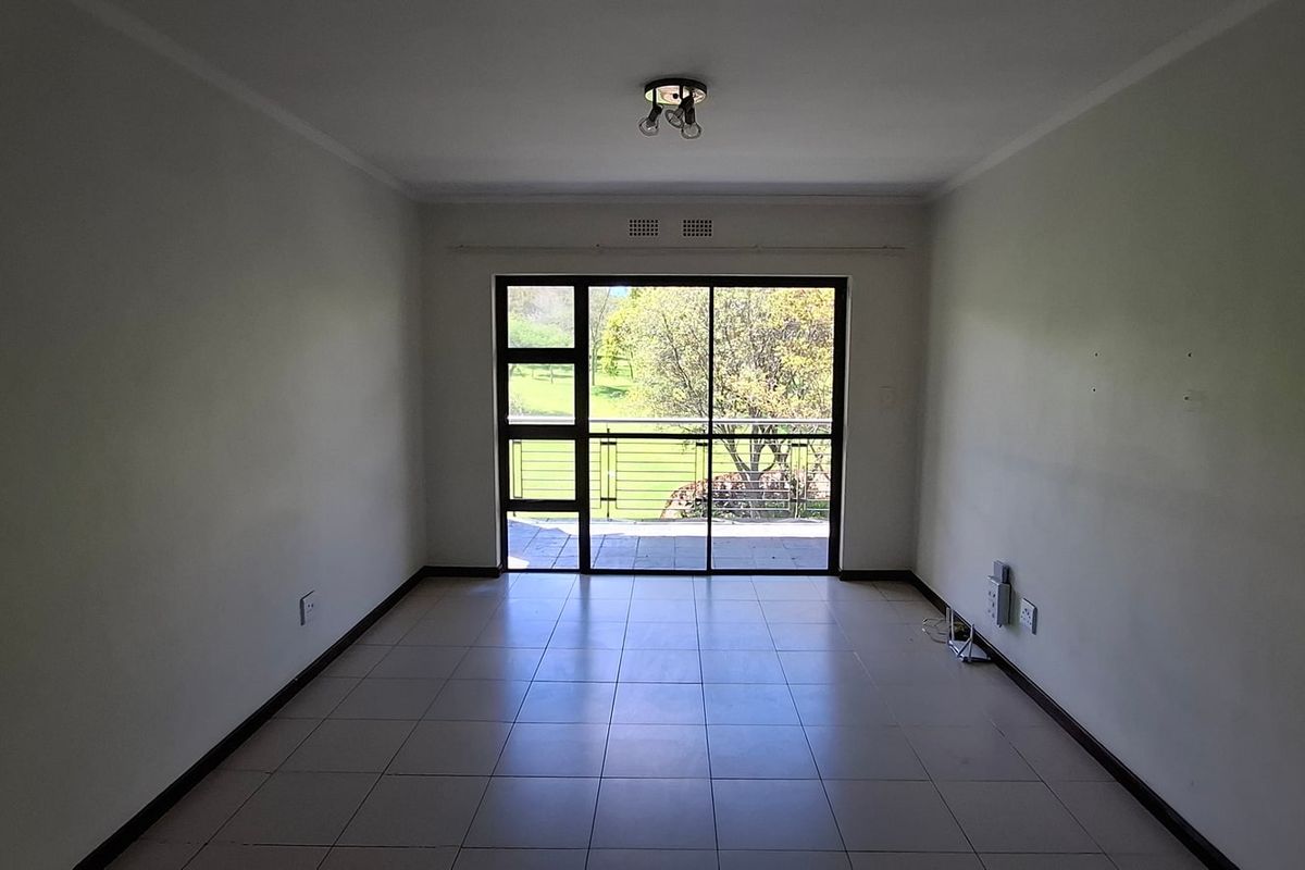 An empty, neutrally painted living room featuring tiled flooring and a large sliding glass door that provides natural light and access to the balcony.