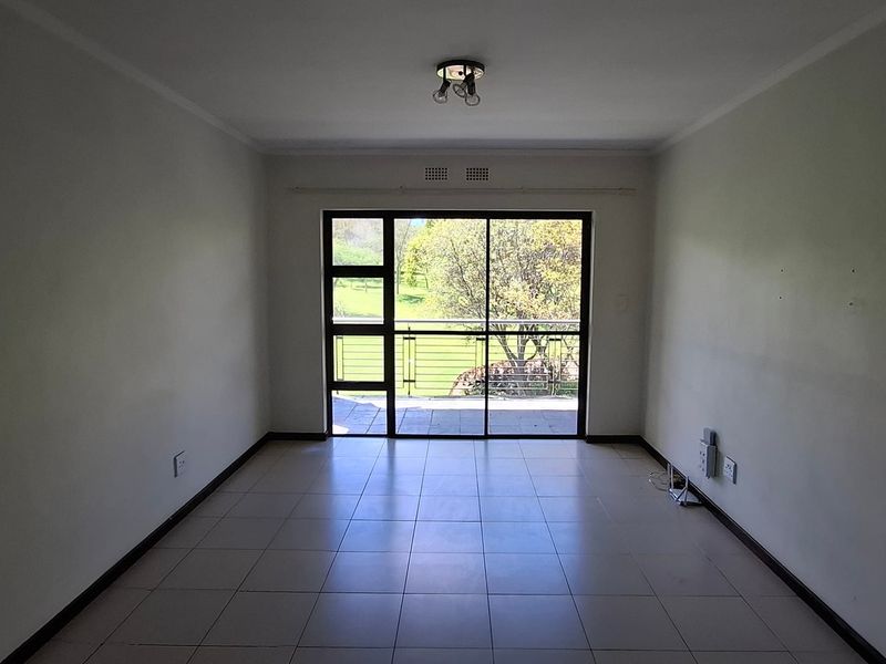 An empty, neutrally painted living room featuring tiled flooring and a large sliding glass door that provides natural light and access to the balcony.