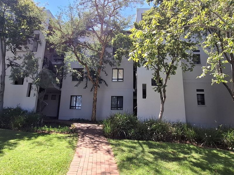 A view of the rear apartment building facade featuring a paved walkway leading through a well-maintained landscaped garden area.