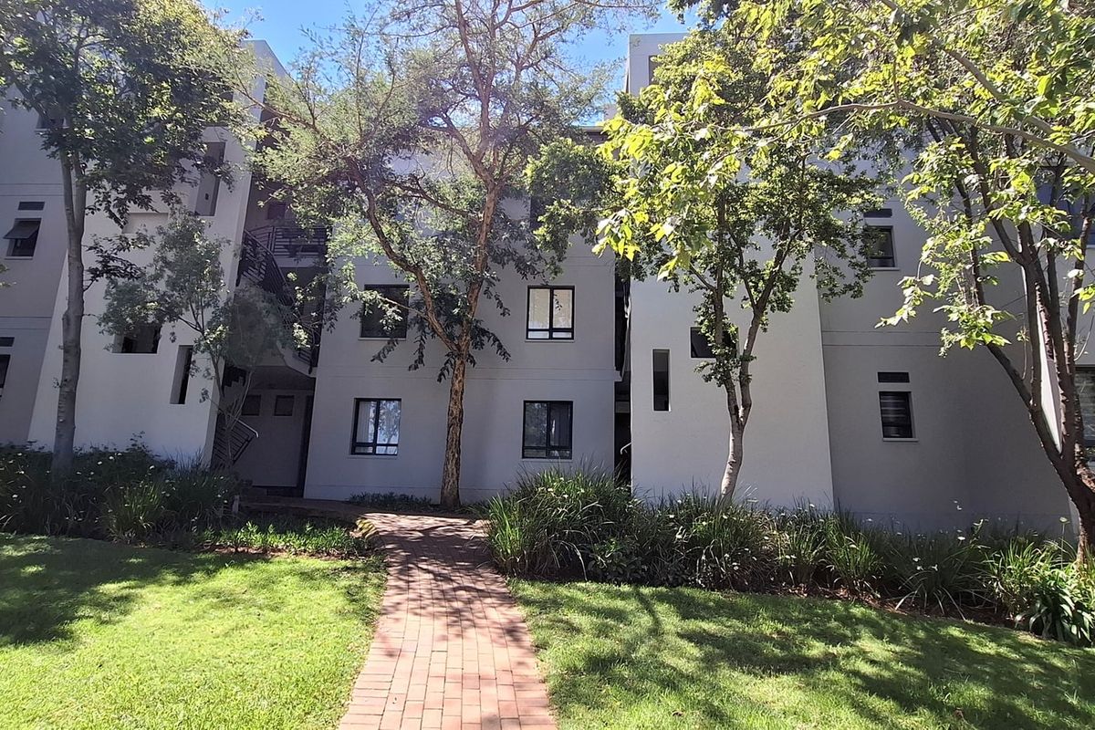 A view of the rear apartment building facade featuring a paved walkway leading through a well-maintained landscaped garden area.