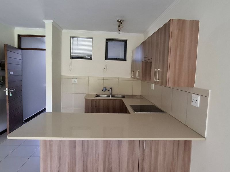 Modern kitchen featuring wood-finish cabinetry, stone countertops, integrated hob, and a dedicated solar inverter and battery system for energy efficiency.