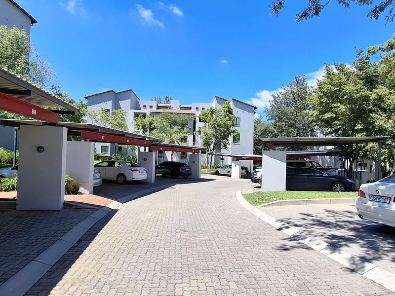 Exterior view of the apartment complex featuring paved driveway access and multiple covered parking bays with concrete structural supports.