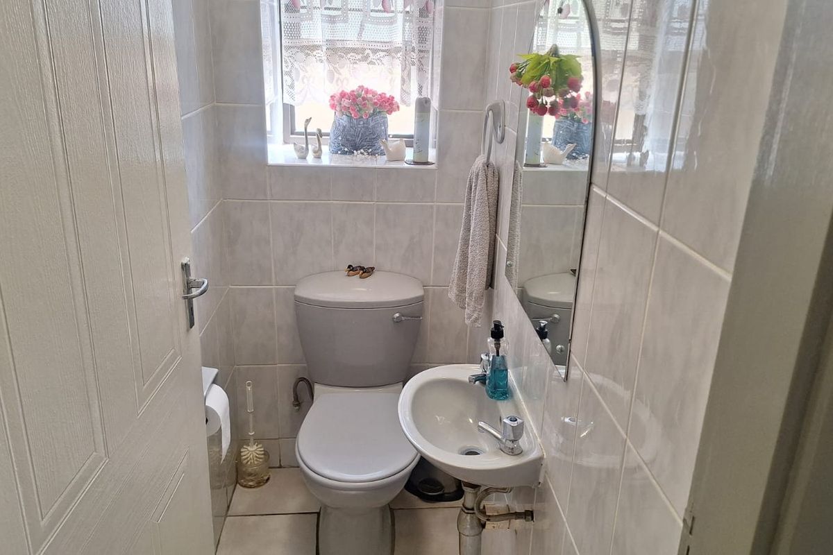 A compact guest bathroom featuring tiled walls and flooring, a wall-mounted basin, and a standard toilet.
