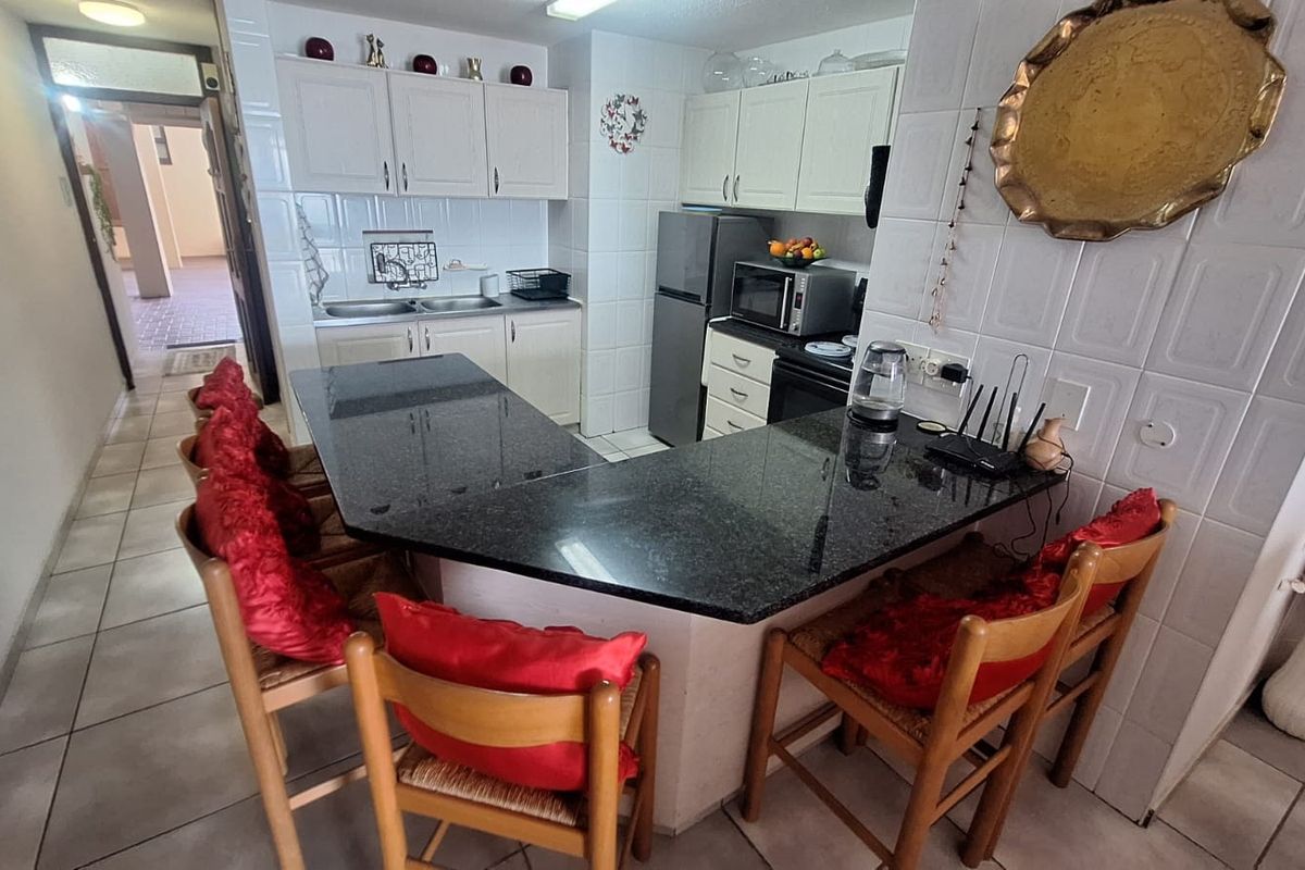 A functional kitchen featuring a U-shaped granite breakfast bar, white cabinetry, tiled backsplash, and ceramic flooring, providing a practical layout for cooking and dining.