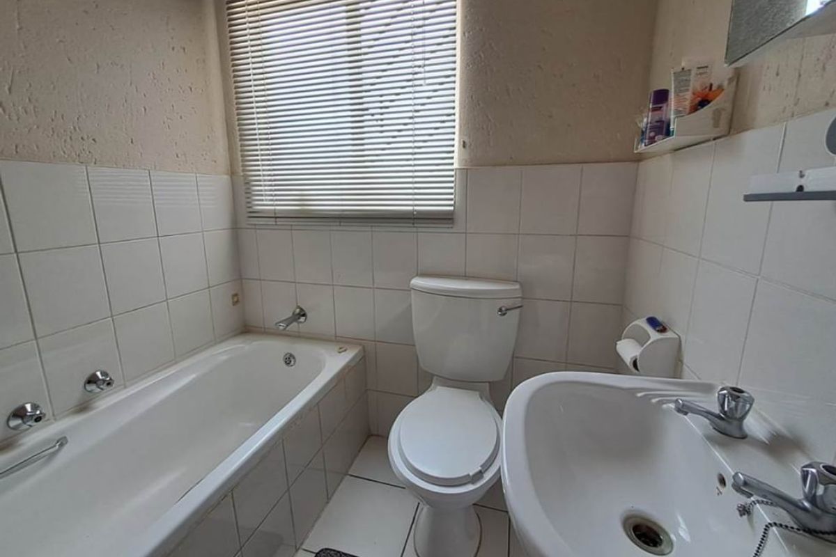 A compact bathroom featuring a standard bathtub, pedestal basin, and toilet with dated wall tiles and neutral finishes, ready for modernization.