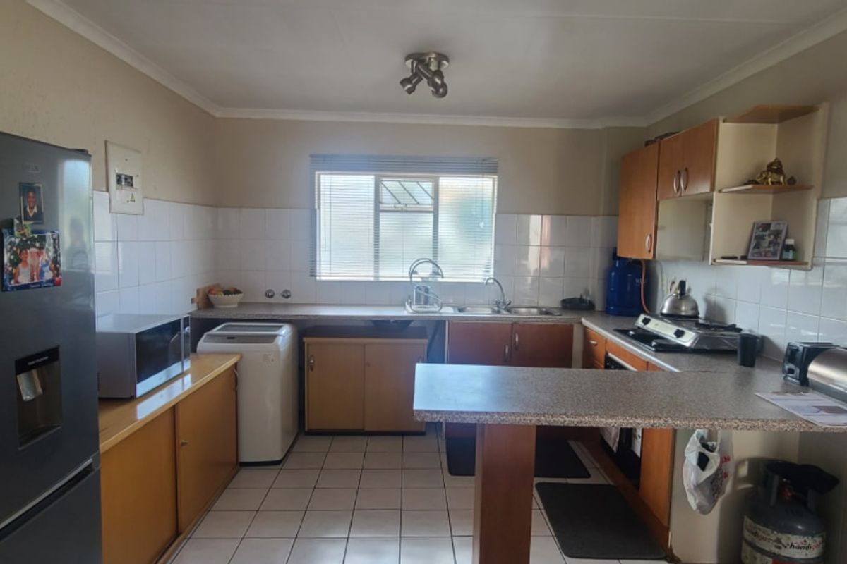 Functional kitchen featuring laminate cabinetry, tiled splashbacks, a breakfast bar, and integrated cooking appliances, offering a practical layout for daily meal preparation.