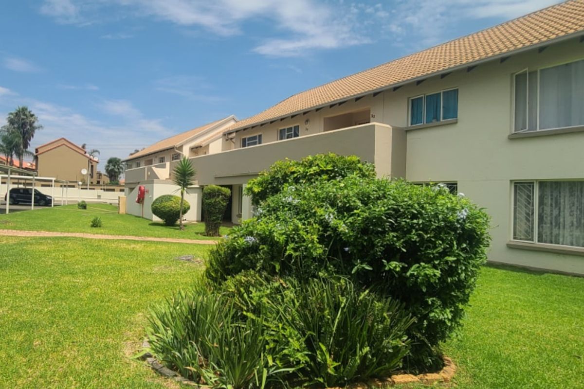 A view of the rear elevation of the apartment complex, featuring a well-maintained lawn, landscaped garden, and balcony access.