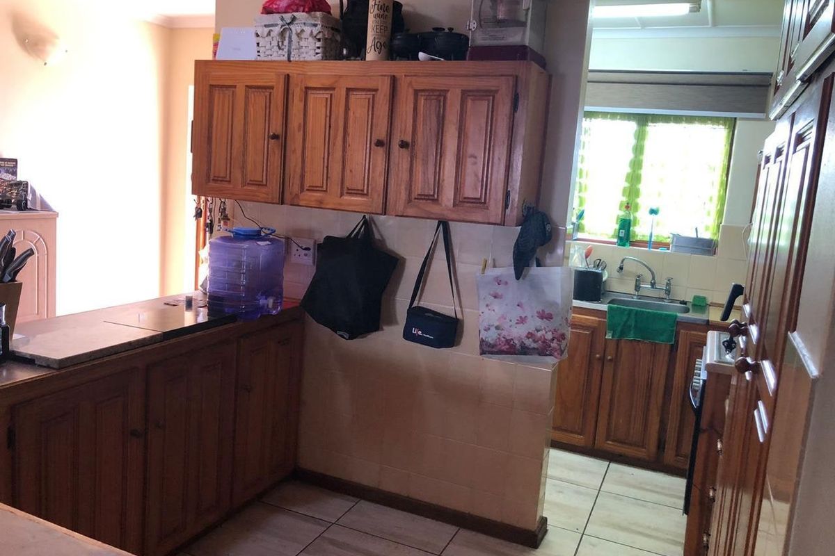 A dated kitchen featuring wooden cabinetry, tiled flooring, and a functional sink area with natural light from a window.