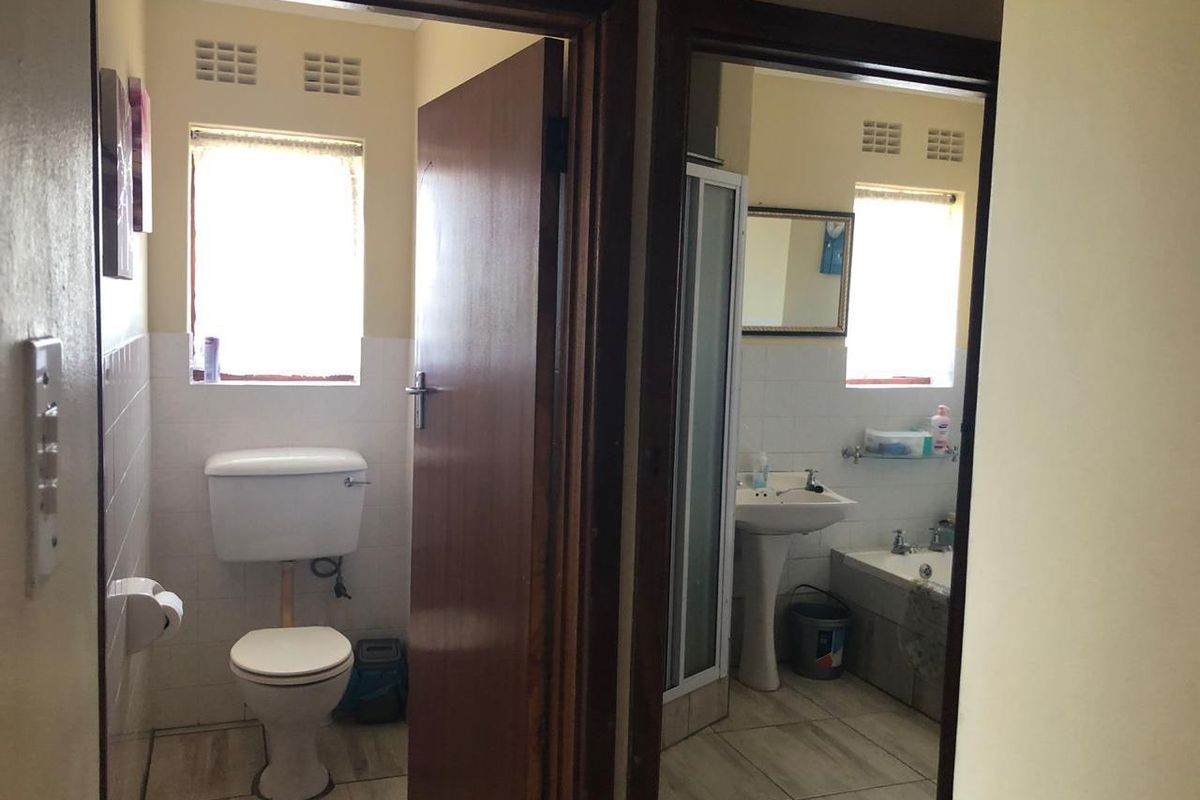 A functional bathroom featuring a separate toilet area, pedestal basin, shower enclosure, and bathtub with tiled finishes and natural light.