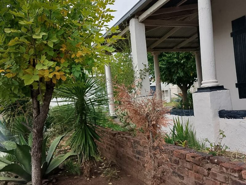 A view of the front facade featuring a covered veranda with classical columns and a low brick retaining wall in the garden.