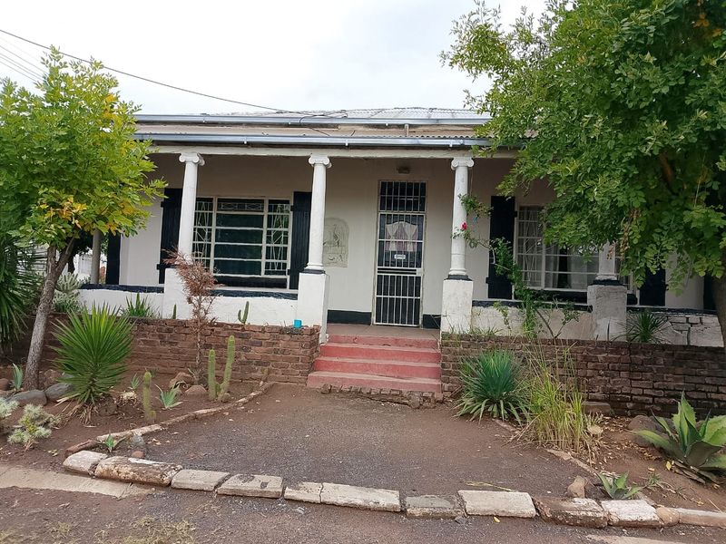 A classic single-story residence featuring a covered front porch with decorative columns, brick retaining wall, and established garden frontage.