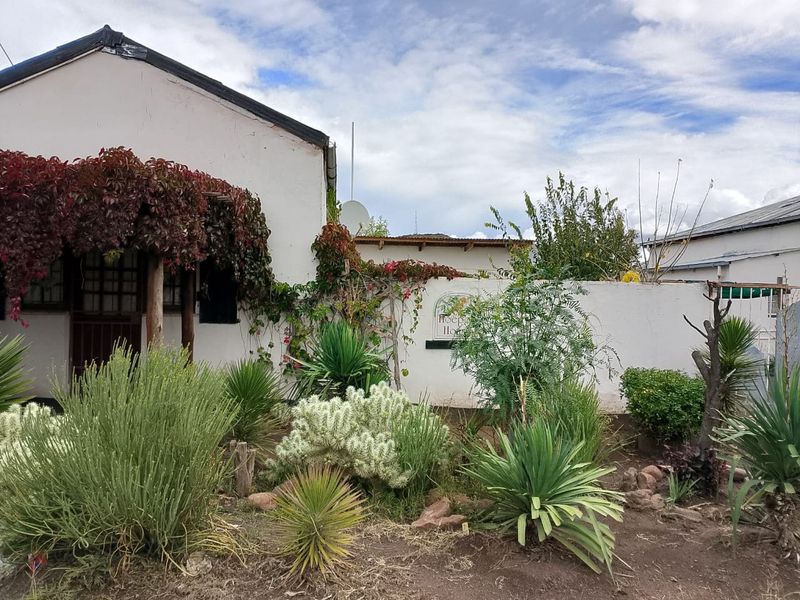 A view of the property's exterior facade featuring a covered entrance area and a landscaped garden with established plants and shrubs.