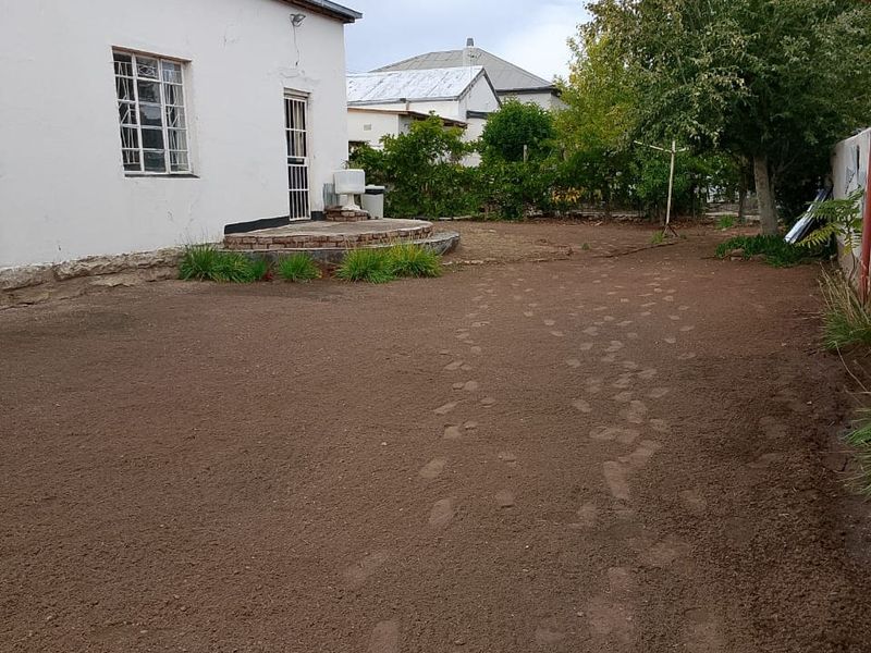A view of the rear exterior of the house featuring a large, unlandscaped backyard area with bare soil and a small paved patio section.
