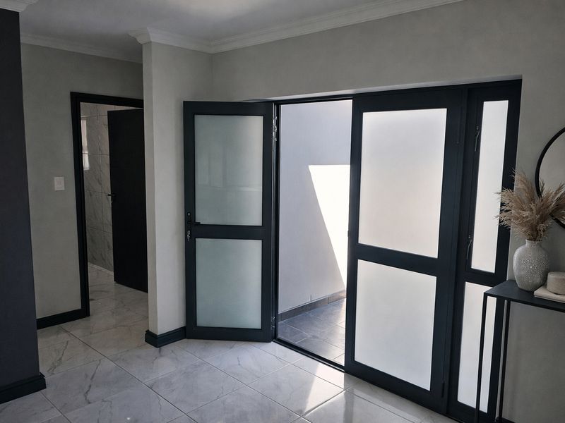 Modern living area featuring high-quality marble-look floor tiles, coving, and contemporary frosted glass double doors leading to an outdoor space.