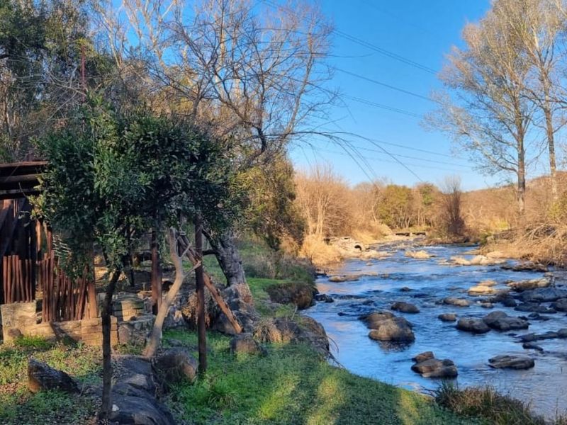 A scenic view of a natural river flowing through the property, featuring a rocky riverbed and mature surrounding trees.