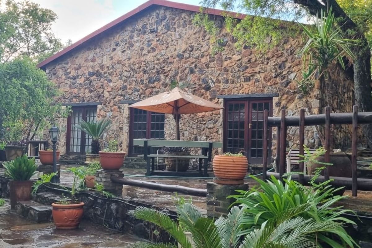 A rustic stone-clad farmhouse exterior featuring a paved patio area, timber-framed doors, and a natural stone retaining wall set within a lush garden.