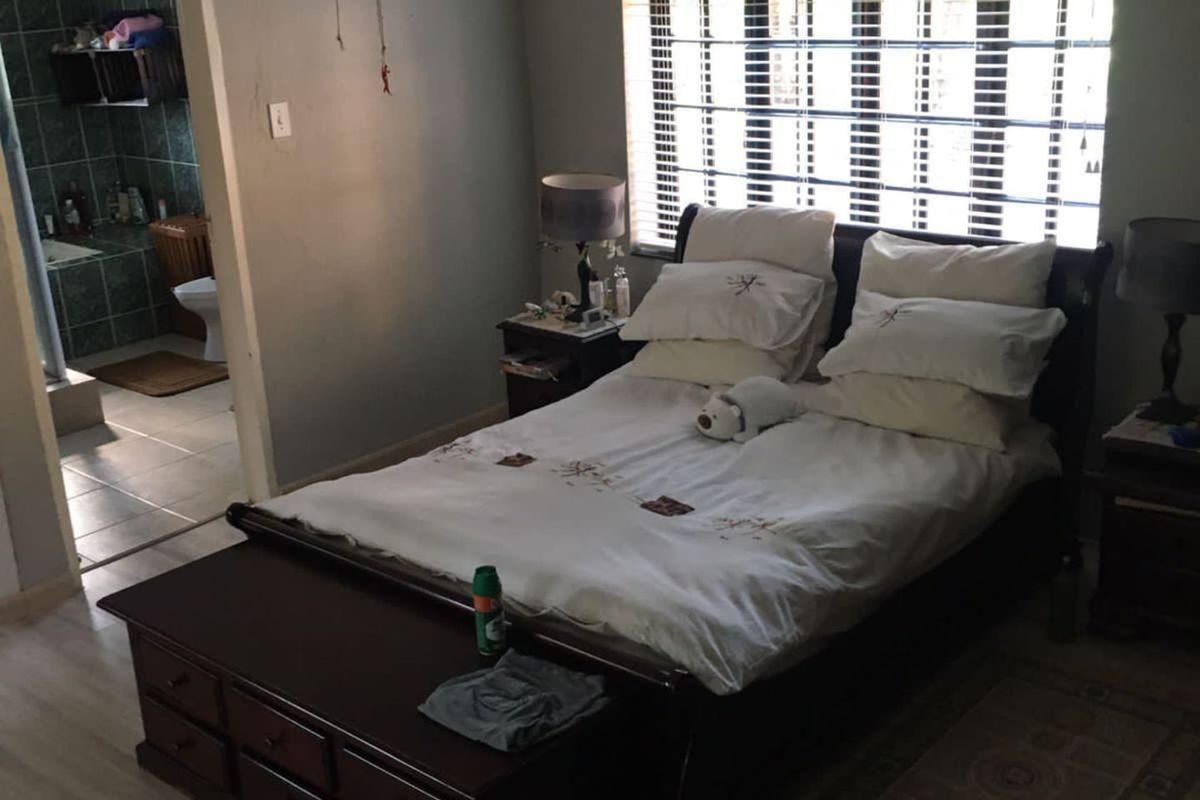 Spacious bedroom featuring laminate flooring, a ceiling fan, and venetian blinds, with an adjoining en-suite bathroom.