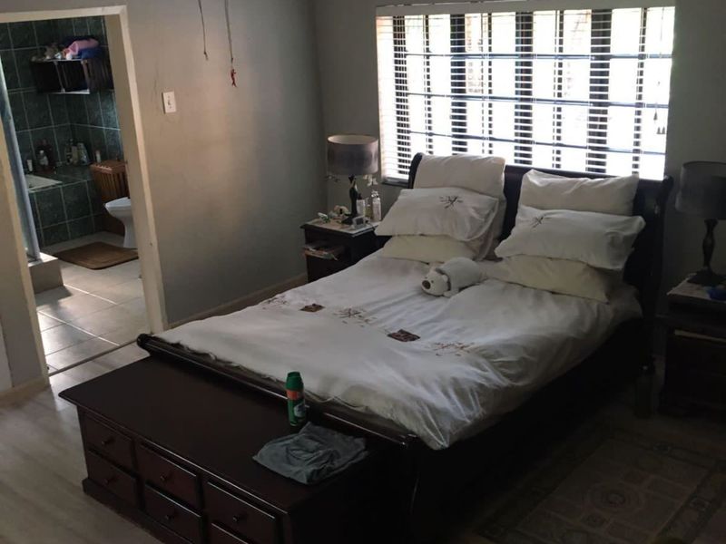 Spacious bedroom featuring laminate flooring, a ceiling fan, and venetian blinds, with an adjoining en-suite bathroom.