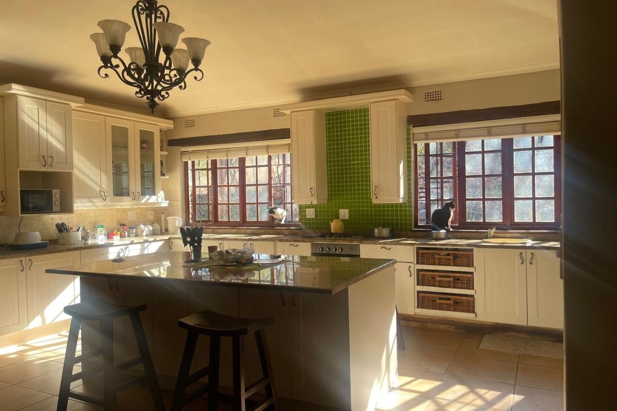 Spacious farmhouse-style kitchen featuring a central island, granite countertops, green tiled backsplash, and ample built-in cabinetry with timber-framed windows.