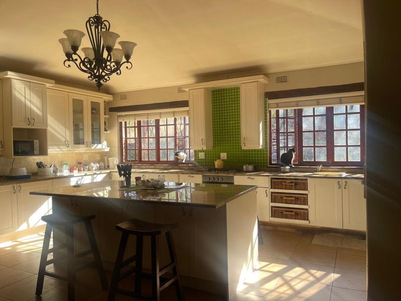 Spacious farmhouse-style kitchen featuring a central island, granite countertops, green tiled backsplash, and ample built-in cabinetry with timber-framed windows.