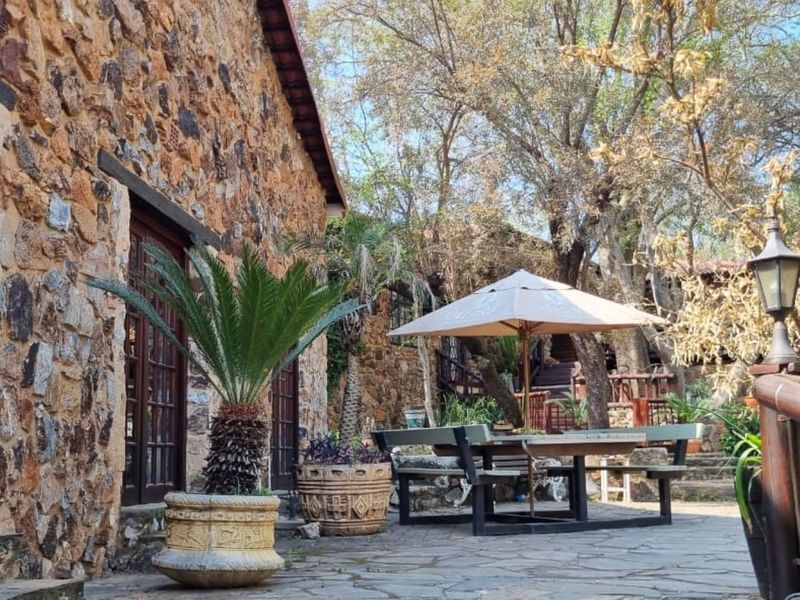 A rustic outdoor patio area featuring natural stone wall cladding, flagstone flooring, and timber-framed glass doors leading into the residence.