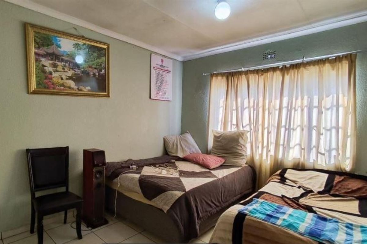 A bedroom featuring tiled flooring and coved ceilings, currently utilized with multiple beds. The space requires cosmetic updates to improve its overall condition.