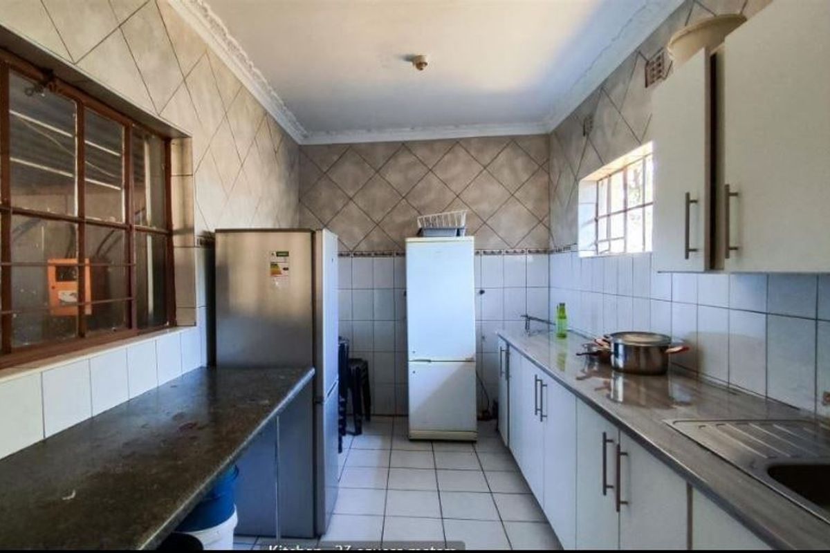 A functional kitchen featuring tiled walls and flooring, laminate countertops, and ample built-in cabinetry, offering a practical space for culinary activities.